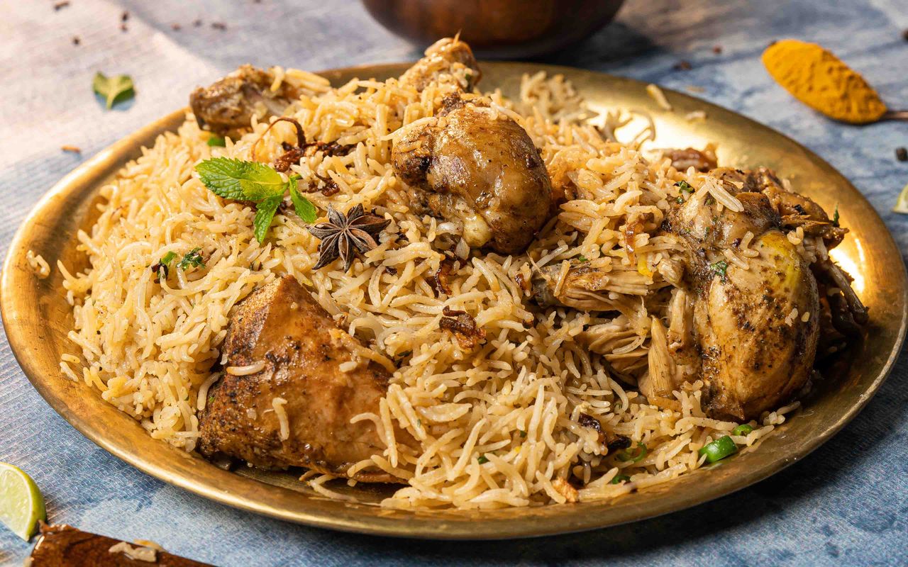 Services Close-up of aromatic chicken biryani served on a brass plate with garnishes, showcasing Indian culinary art.