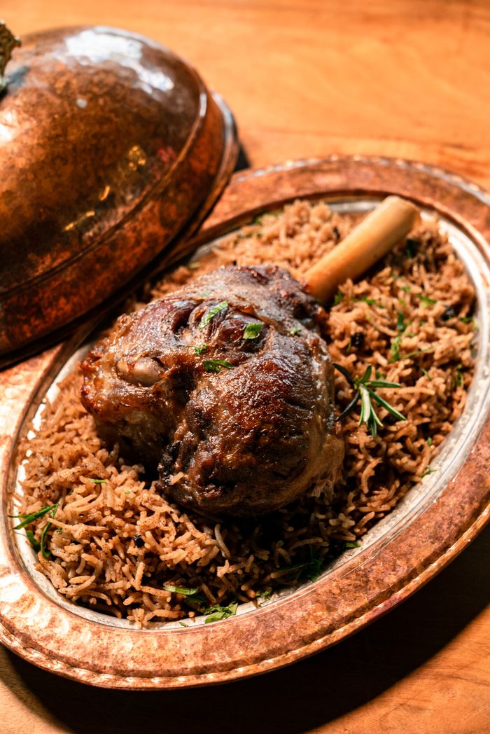 Deliciously roasted lamb shank served on a bed of aromatic rice in a copper dish.